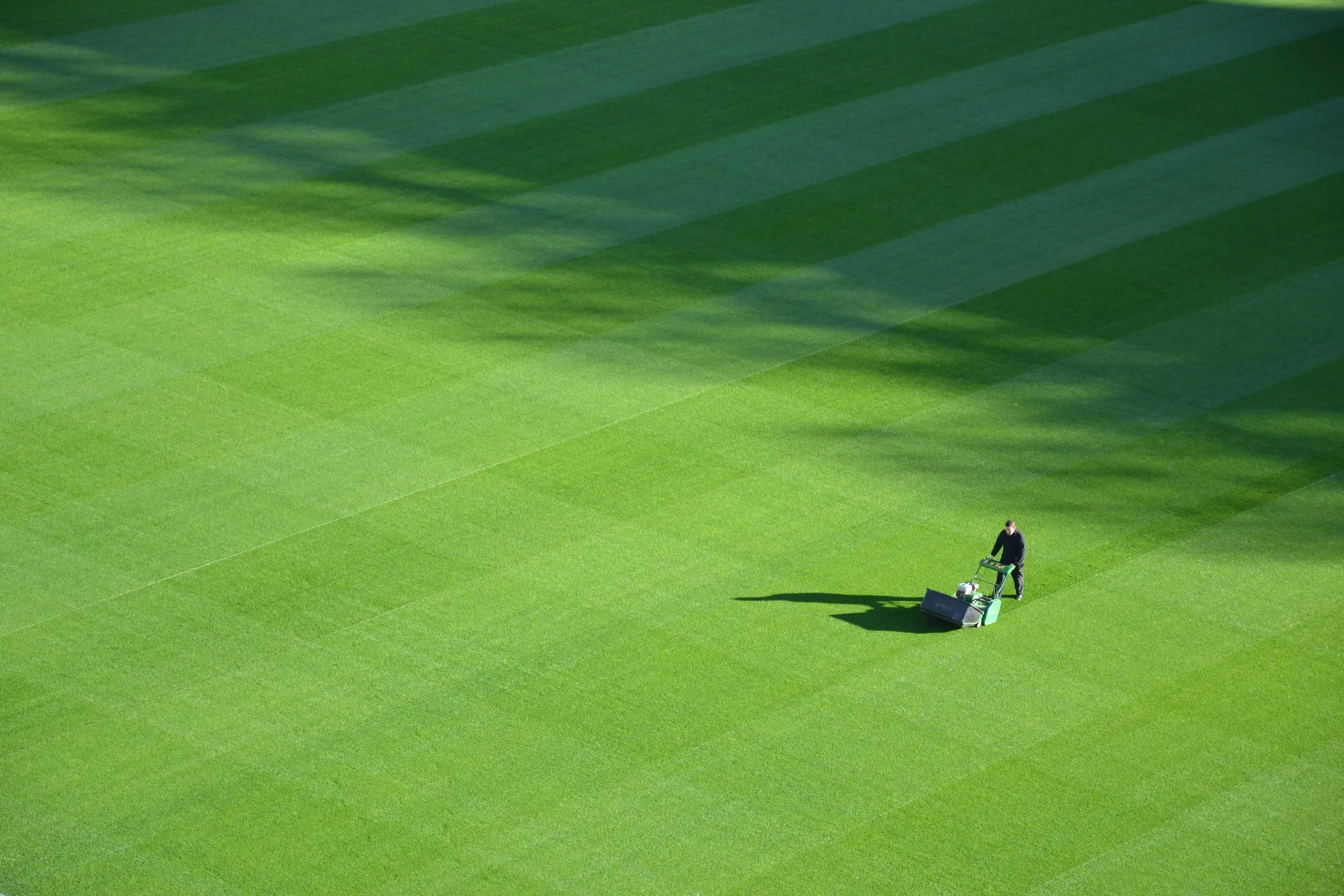 Een terreinverzorger maait een gestreept grasveld, van boven gezien